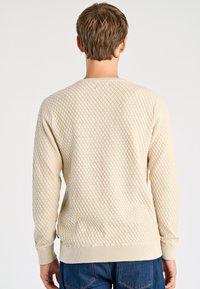 Beige-texturoitu pusero, jossa timanttikuosi, resorit hihansuissa ja helmassa, pyöreä pääntie ja pitkät hihat.