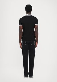 Svart T-skjorte med kontrasterende hvit krage og ermeakenter, sammen med svarte bukser. Skjorten har en logo på kragen.