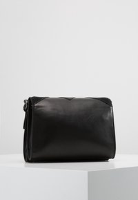 Czarna skórzana torba o prostokątnym kształcie, miękkiej teksturze i zapięciu na klapę. Posiada subtelny pikowany wzór na górze oraz srebrne okucia.