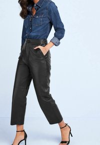 Black leather pants with a high waist and straight leg, featuring two side pockets and a button closure. Paired with a denim shirt.