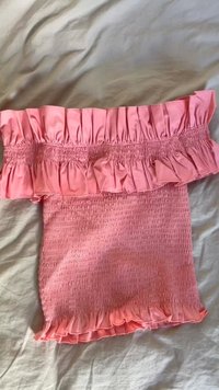 Īss rozā tops ar smockotu ķermeni un ruffled bezpiedurkņu kaklu. Audumam ir gluda tekstūra un viegla sajūta.