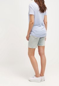 Helles blaues T-Shirt mit kurzen Ärmeln, kombiniert mit verwaschener Jeansshorts. Weiße Sneakers vervollständigen das Outfit.