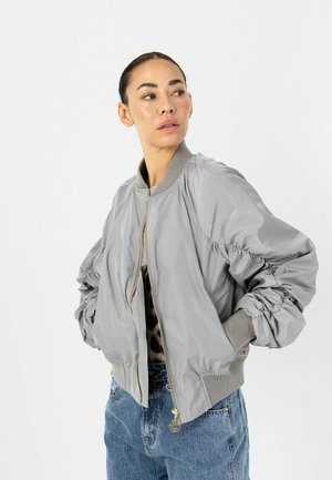 Giacca bomber grigia con maniche arricciate, polsini e collo a coste. Tessuto liscio e leggero con chiusura a zip e lieve lucentezza.