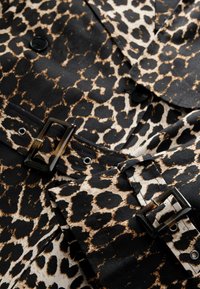 Látka s leopardím potiskem v černé, béžové a hnědé barvě, se černými knoflíky a detaily přezky na pásku, s hladkou texturou.