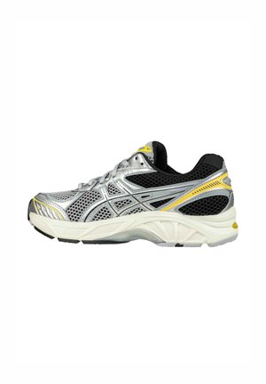 Chaussure de course argentée avec tige en mesh noir, accents jaunes et semelle blanche rembourrée. Présente un design stratifié et des textures contrastées.
