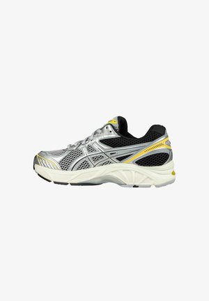 Chaussure de course argentée avec tige en mesh noir, accents jaunes et semelle blanche rembourrée. Présente un design stratifié et des textures contrastées.
