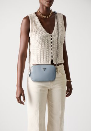 Small light blue leather crossbody bag with silver hardware, rectangular shape, and a textured finish. Worn with a knitted cream top.