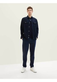 Chemise button-up bleu marine avec deux poches avant, associée à un pantalon bleu marine assorti et des baskets blanches. Tissu décontracté et coupe droite.