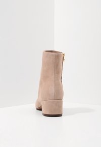 Botín de ante en beige claro con tacón cuadrado. Presenta una cremallera lateral y una textura suave. Punta redondeada y diseño minimalista.