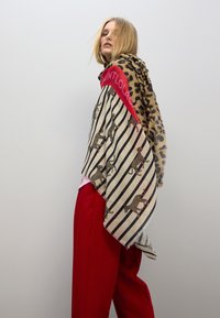 Chal con una mezcla de estampados de leopardo y rayas. Tejido suave y ligero con bordes deshilachados y un acento rojo audaz en la parte superior.