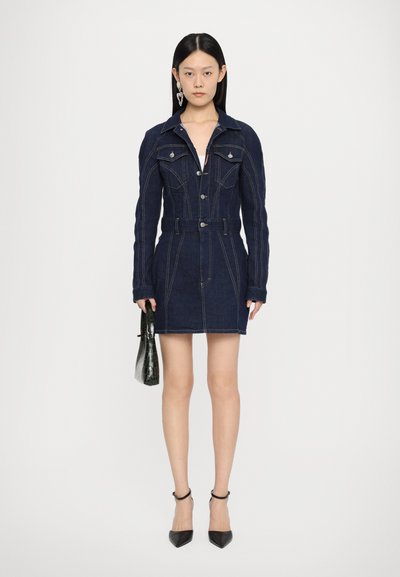 Dark denim dress with long sleeves, pointed collar, front buttons, and an adjustable waist belt. Worn with black heels and a small bag.
