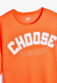 Orange atletisk t-shirt lavet af åndbart stof, med rund halsudskæring og fed hvid grafik med teksten "VÆLG AT VÆRE GLAD."