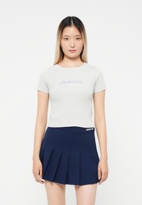 Világosszürke, rövid ujjú póló "Santa Cruz" logóval, navy kék, pliszírozott szoknyával párosítva, amelynek derékrészén Adidas logó található.