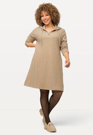 Abito beige con cappuccio in tessuto a coste, caratterizzato da un colletto con zip e maniche a tre quarti, abbinato a scarpe chunky chiare.
