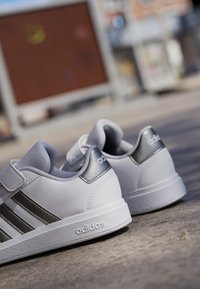 Bijele Adidas tenisice imaju glatku kožnu gornjište, srebrne akcentne detalje, tri crne pruge i teksturiranu gumenu potplat koja osigurava prianjanje.