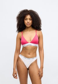 Rozā bralette ar plānām siksnām un baltu lentes joslu, kurā ietverts "Calvin Klein" logotips; apvienots ar baltām tanga apakšbiksēm ar atbilstošu jostu. Gluda auduma.