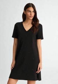 Rochie neagră cu decolteu în V, realizată dintr-un material moale, cu mâneci scurte și embellismente într-un model simetric pe partea din față.