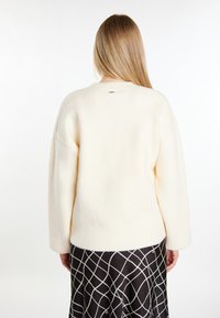 Kremowy, oversize'owy sweter z okrągłym dekoltem i długimi rękawami, wykonany z miękkiego materiału, pokazany z tyłu.