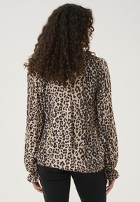 Halenka s leopardím vzorem z lehkého materiálu, s dlouhými rukávy, nařasenými manžetami a volným střihem. Světle béžová a černá barevná kombinace.