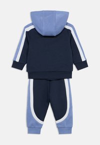 Μπλε ναυτικό και ανοιχτό μπλε φόρμα με κουκούλα, με λευκές πλευρικές ρίγες τόσο στο σακάκι όσο και στο παντελόνι, κατασκευασμένη από μαλακό βαμβακερό υλικό.