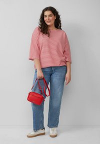 Rood en wit gestreepte oversized top, blauwe jeans en witte sneakers met lichtbeige accenten. Bevat een kleine rode crossbody tas.