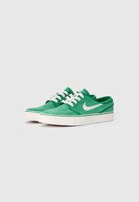 Zelene platnene tenisice s bijelim vezicama, bijelim Nike swoosh logom i zelenim naglascima duž potplata. Jednostavan dizajn s vidljivim šavovima.