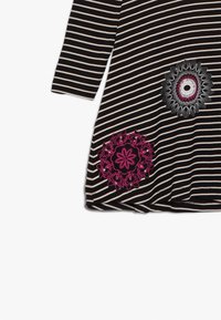 Czarna i biała tunika w paski z rękawami do łokcia, ozdobiona różowo-białym haftem kwiatowym na dolnej prawej stronie.