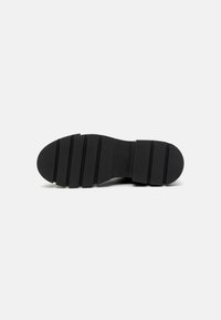 Suela de zapato de goma negra con ranuras horizontales para tracción, punta redondeada y una construcción sólida sin logotipos o adornos visibles.