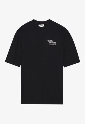 Sort bomuld t-shirt med korte ærmer, en rund halsudskæring og hvid tekst, der står "YEARS/UNFOLDED" på venstre brystområde.