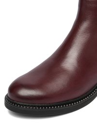 Pruunika nahast pahkluu saabas ümmarguse ninaga, tekstuurse viimistlusega ja dekoratiivse naelutisega serva along sisetalla, mis lisab detaili.