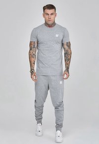Grå bomulds t-shirt og matchende joggingbukser med elastiske manchetter. Har en lille hvid logo på trøjen. Hvide sneakers fuldender outfittet.