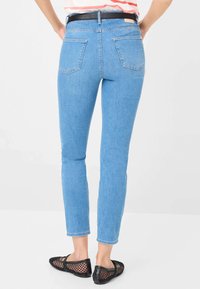 Jean skinny bleu avec un léger stretch, doté d'une taille mi-haute, de poches arrière et d'une texture en denim lisse. Porté avec des chaussures en mesh noires.
