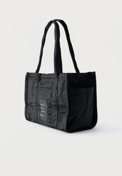 Μαύρη ορθογώνια τσάντα ώμου με επενδυμένες λαβές, κάθετες γραμμές ραφής, εξωτερική πλαϊνή τσέπη και μικρό λευκό πατς με κείμενο στο μπροστινό μέρος.