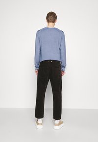 Maglione blu a maglia con texture a coste, abbinato a pantaloni in corduroy neri. Il modello indossa sneaker beige con suola bianca.
