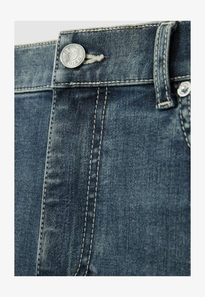 Jean en denim bleu foncé avec une vue rapprochée d'un bouton en métal, des coutures contrastées et une texture lisse, mettant en valeur la taille et les détails de couture.