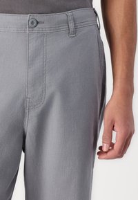 Gray pants made of woven fabric, featuring a button closure, flat front, and side pockets. Seam detailing adds texture.