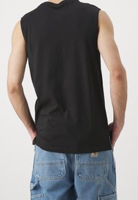 Svart ärmlös skjorta i bomull, med avslappnad passform och rund halsringning. Matchas med blå denim cargo byxor med fickor.