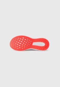 Semelle de chaussure de sport en caoutchouc rouge et blanc. Dispose d'une surface texturée avec des motifs circulaires et des rainures pour l'adhérence.