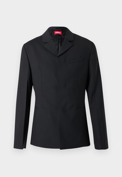 Blazer noir ajusté avec revers crantés, boutonnage simple, poches à welt, et étiquette rouge 032c à l'intérieur du col.
