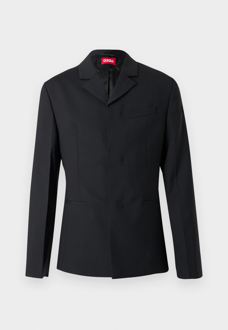 Sort skræddersyet blazer med hakkede revers, enkeltspændt front, skrålommer og rød 032c-label indeni kraven.