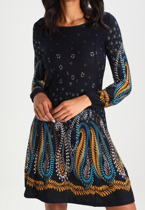 Långärmad klänning i mörk marinblå med blommiga och paisleymönster i turkos, guld och grått. Har en åtsittande bodice och en utsvängd kjol.