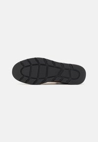 Semelle en caoutchouc noir d'une chaussure avec des motifs de bande de roulement profonds et le logo Levi's embossé près du talon.