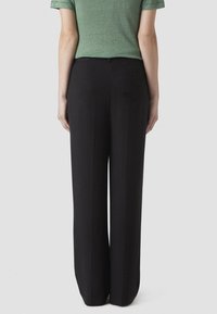 Svarta vida byxor i mjukt material, med hög midja och en diskret bakficka. Designen är minimalistisk med en skräddarsydd passform.