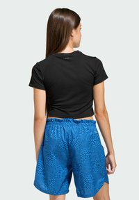 Crni skraćeni T-shirt s kratkim rukavima, uparen s kratkim hlačama u plavom leopard uzorku, koje imaju elastičnu traku u struku i teksturirani materijal.