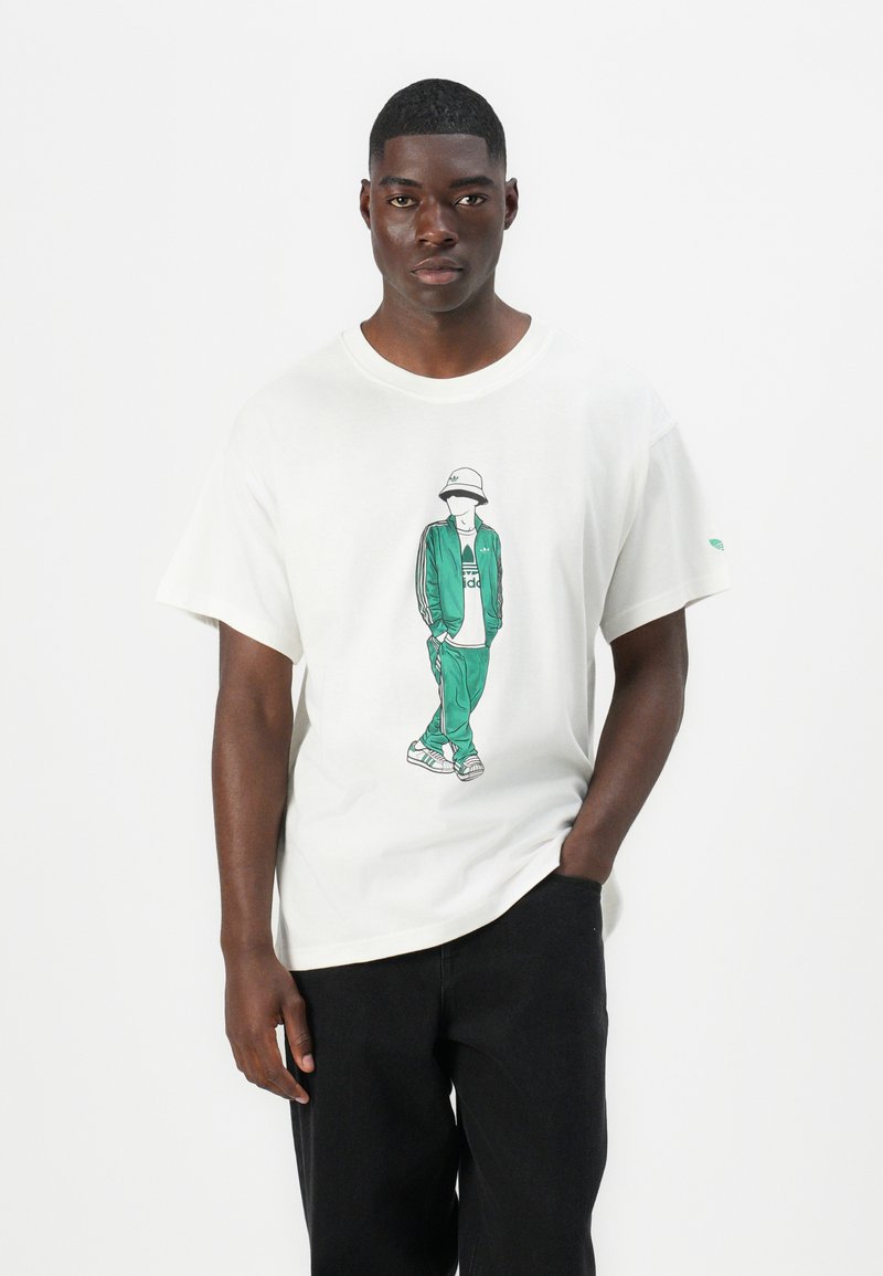 Biała bawełniana koszulka z grafiką postaci w zielonym dresie i kapeluszu typu bucket. Luźny krój, krótki rękaw i okrągły dekolt.