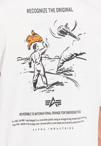 Witte t-shirt met een zwarte illustratie van een persoon die een oranje jack vasthoudt, met daaronder tekst over de geschiedenis van het MA-1 jack.