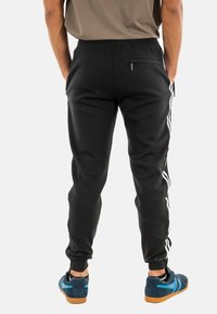 Zwarte joggings met witte zijstrepen, taps toelopend ontwerp, verstelbare tailleband en een achterzak. De stof lijkt zacht en textuur te hebben.