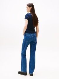 Marineblå tettsittende t-skjorte kombinert med høy livvidde, løse blå denimjeans med baklommer og svart fottøy. Enkel, minimalistisk design.