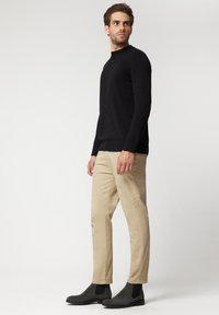 Czarny sweter z długim rękawem i wysokim kołnierzem, zestawiony z beżowymi spodniami i czarnymi botkami za kostkę. Gładkie tekstury w całym zestawie.