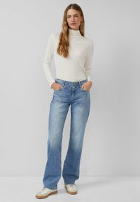 Dopasowany biały top z golfem w połączeniu z niebieskimi, szerokimi dżinsami o wyblakłym odcieniu, z przednimi kieszeniami i zapięciem na guziki.